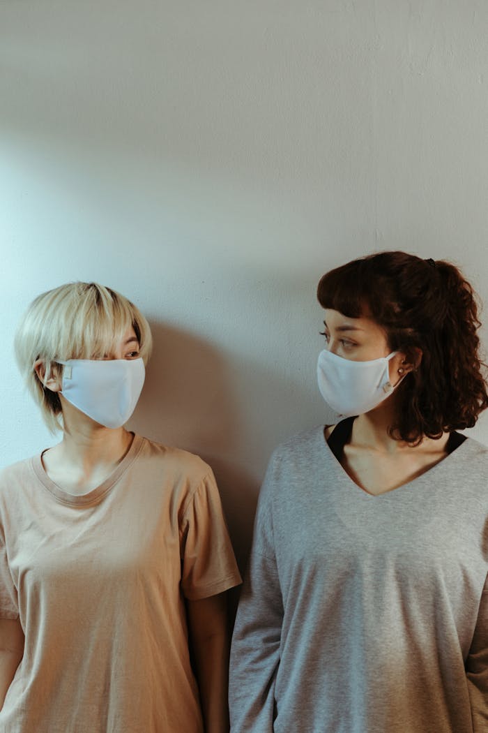 Two women wearing masks stand indoors, maintaining social distance during a pandemic.